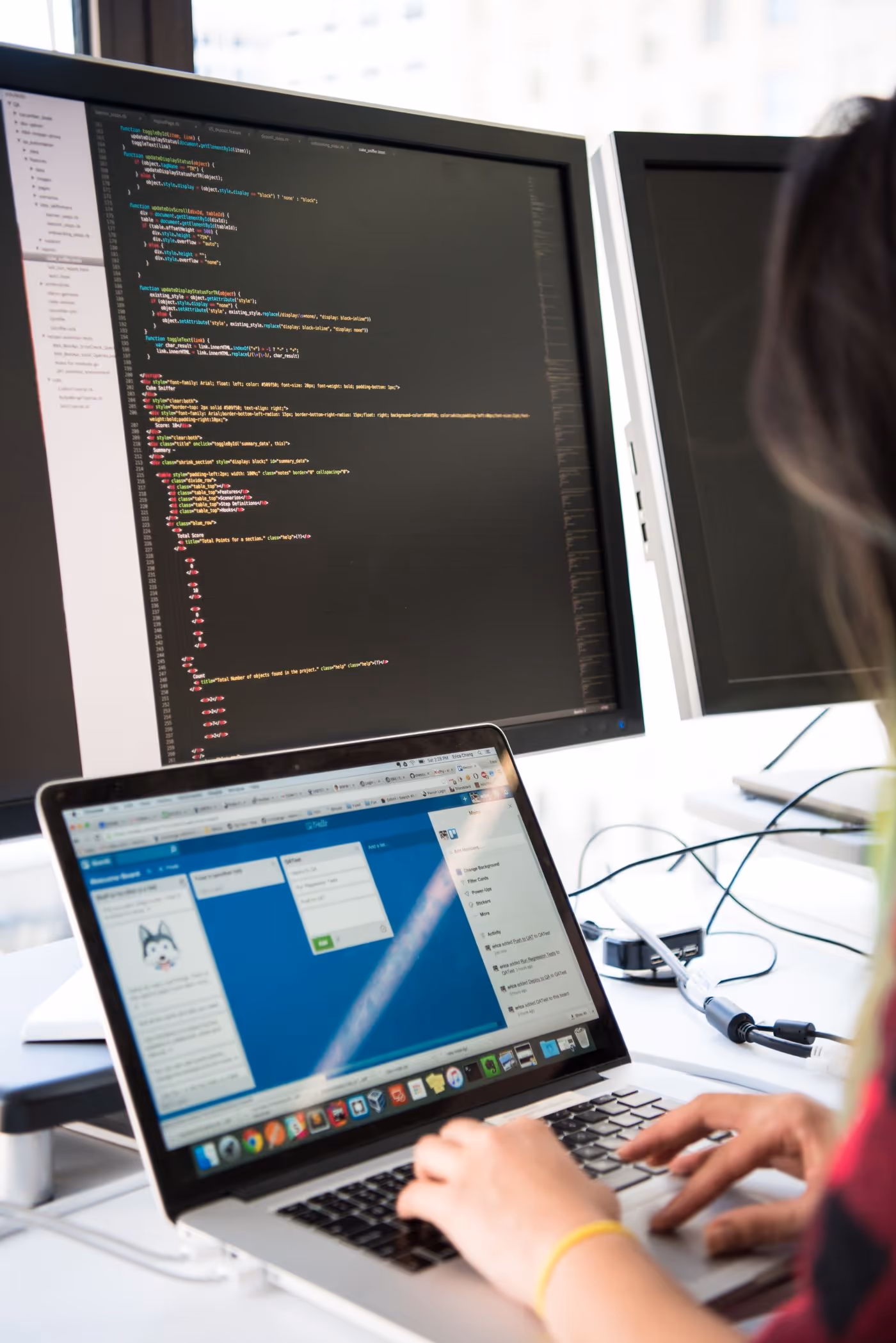 Developer typing on a laptop in front of monitors showing code