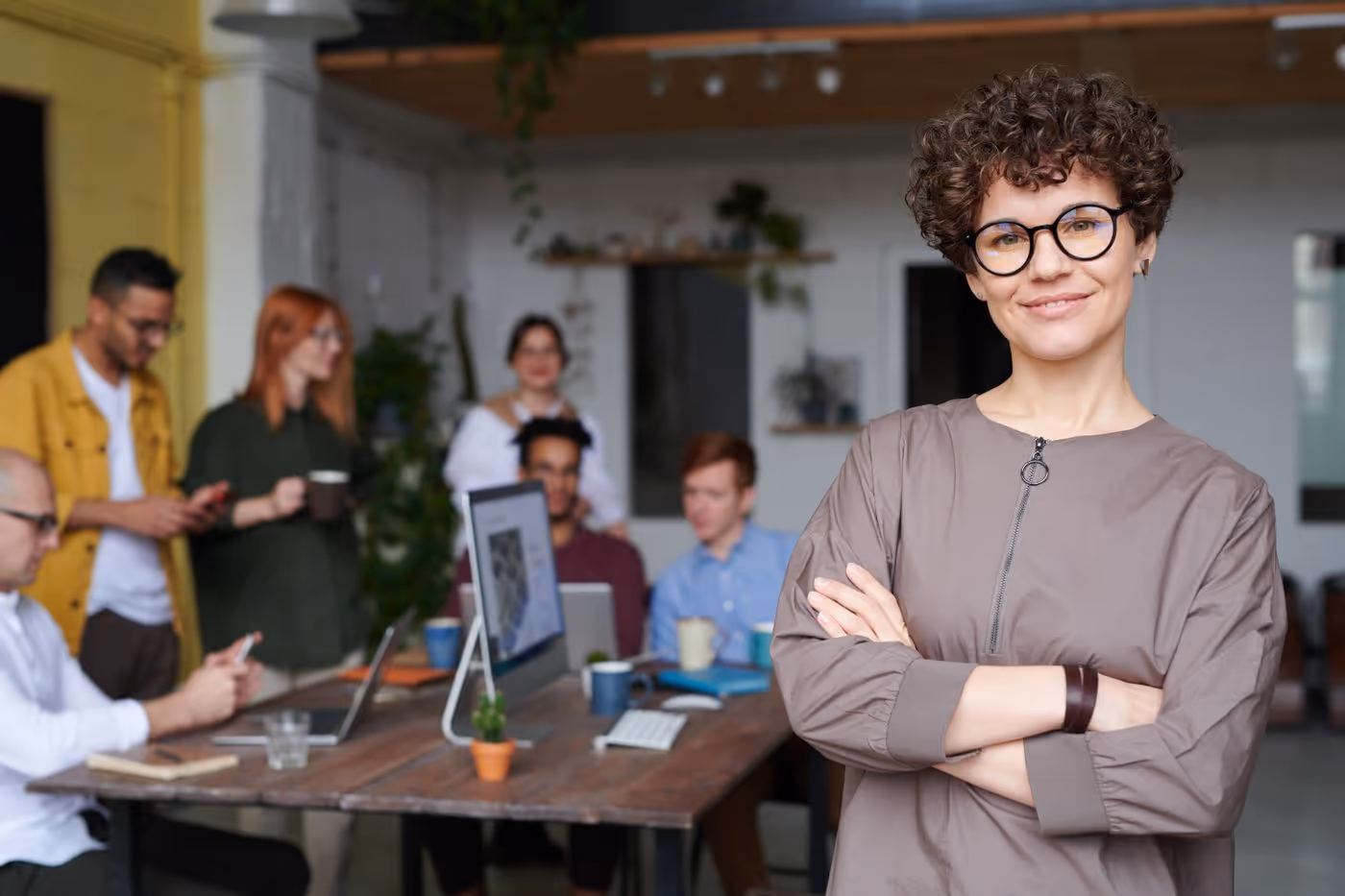 Woman with arms crossed in an office while her team works behind her
