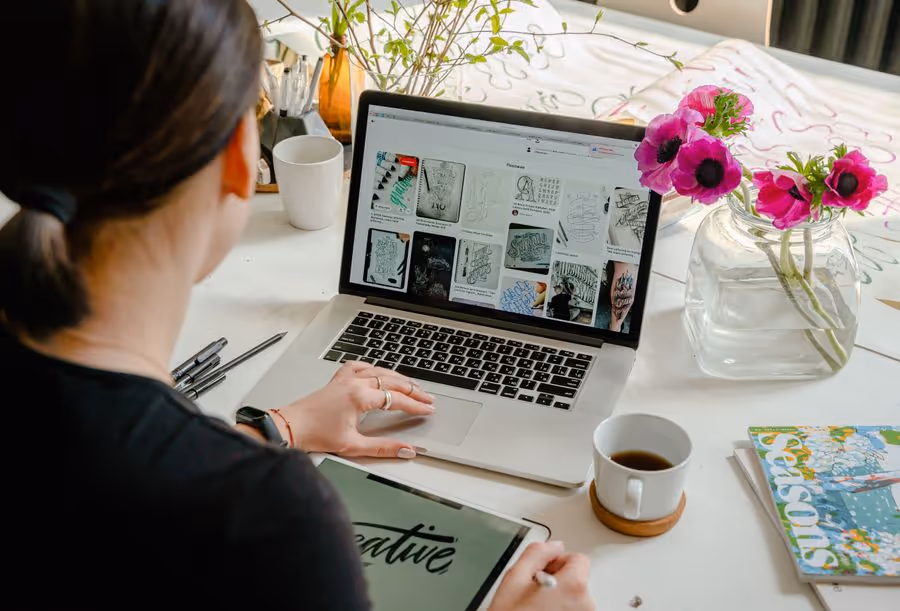 Designer working on a laptop at a desk with flowers, coffee and a tablet