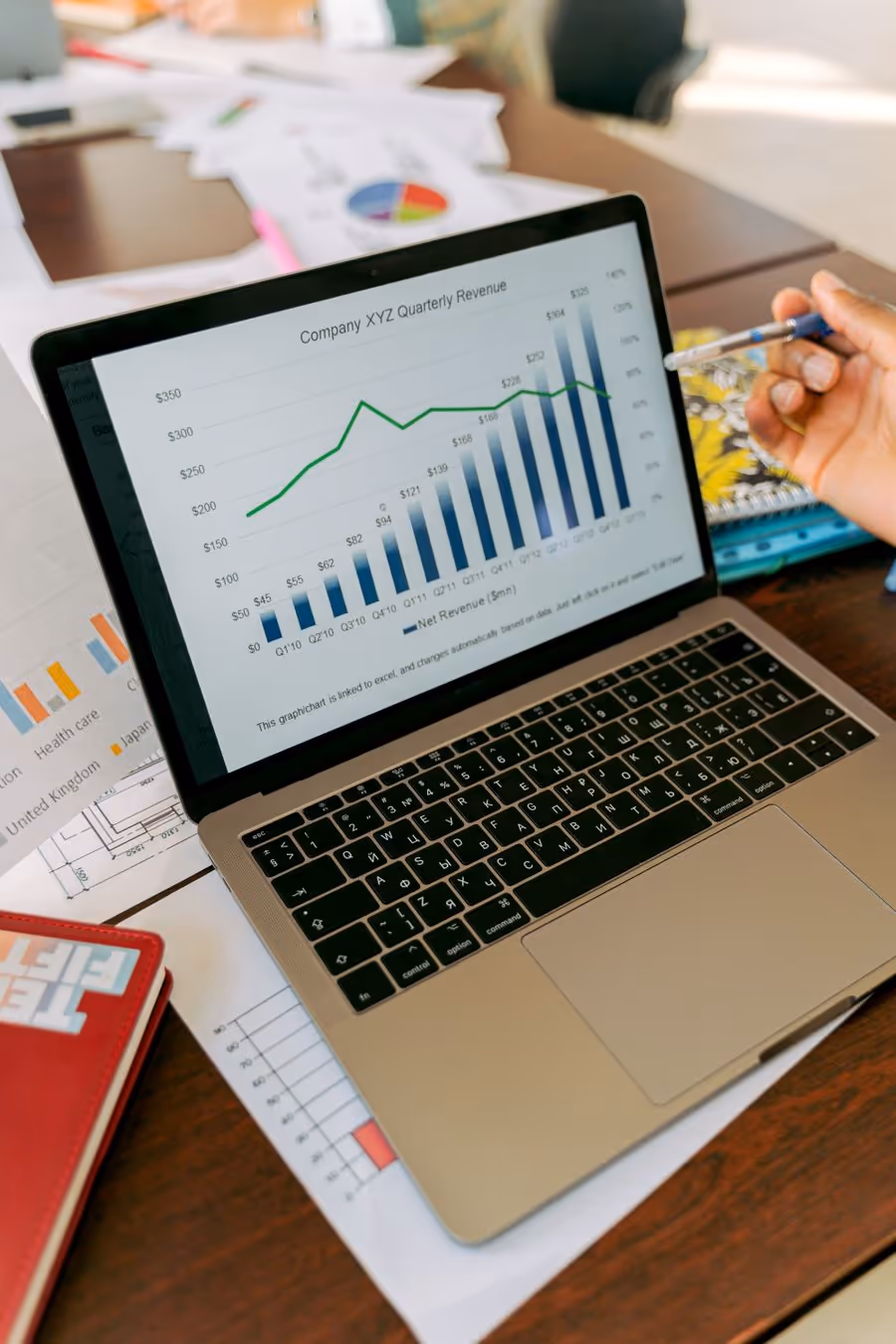 Laptop showing a revenue bar chart on a desk covered in printed reports