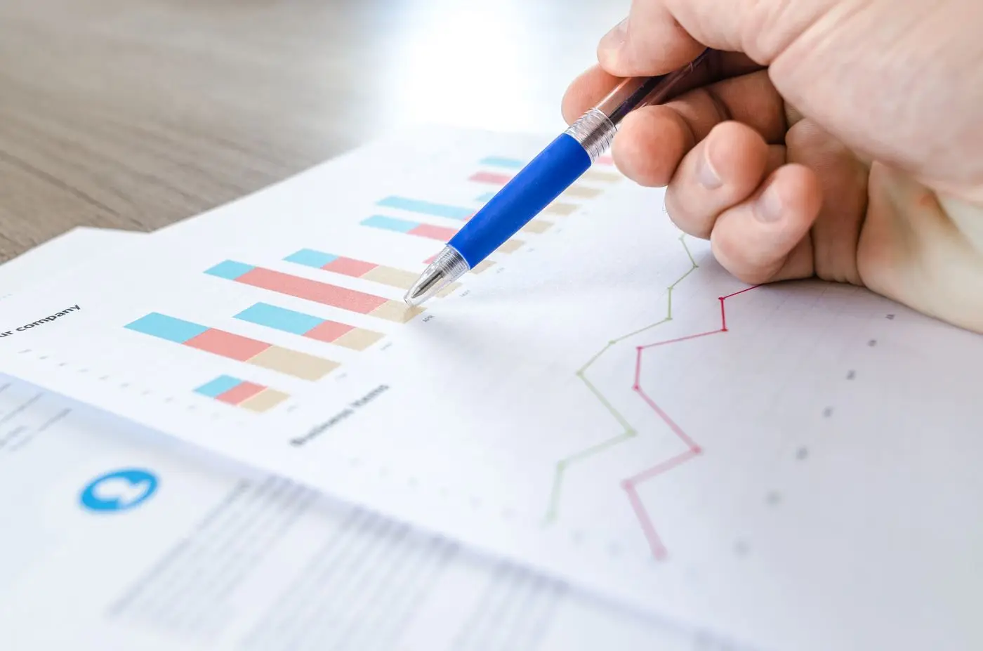 Hand with a pen pointing at bar and line charts on a printed report