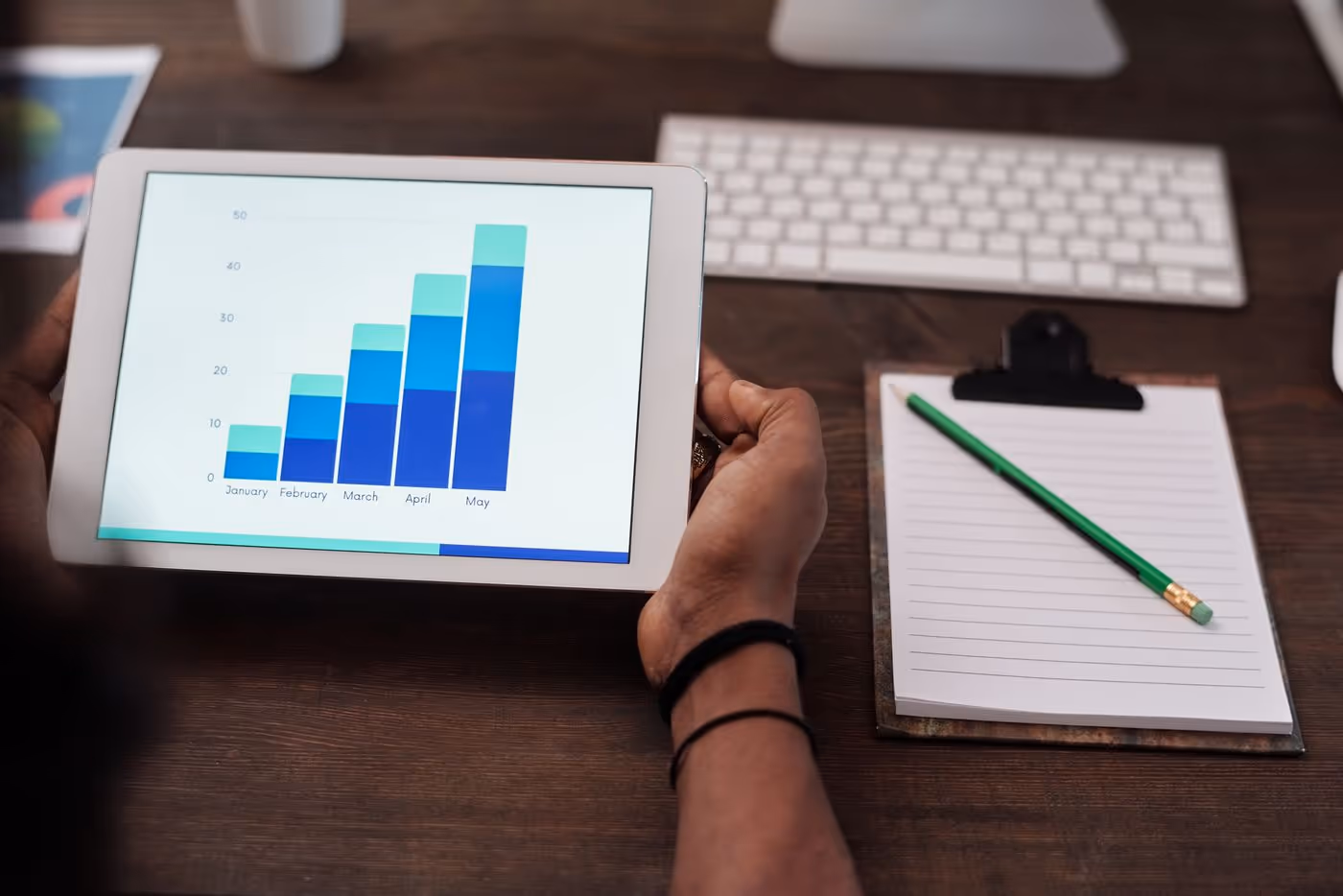 Hands holding a tablet that shows a monthly bar chart