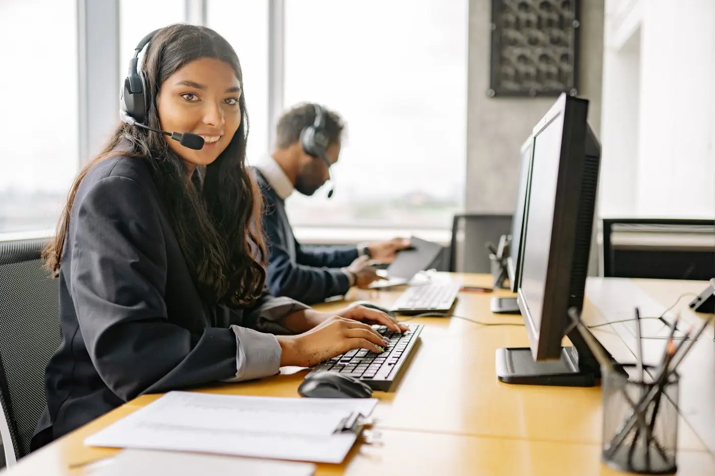 Smiling support agent with a headset working at a computer
